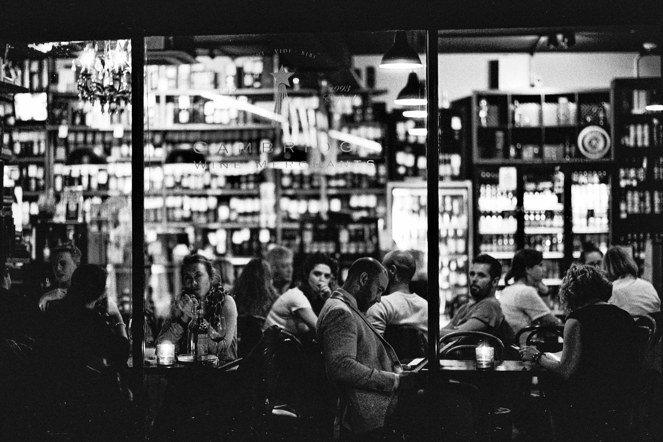 People sitting in a warmly lit café, seen through the glass from the dark street outside