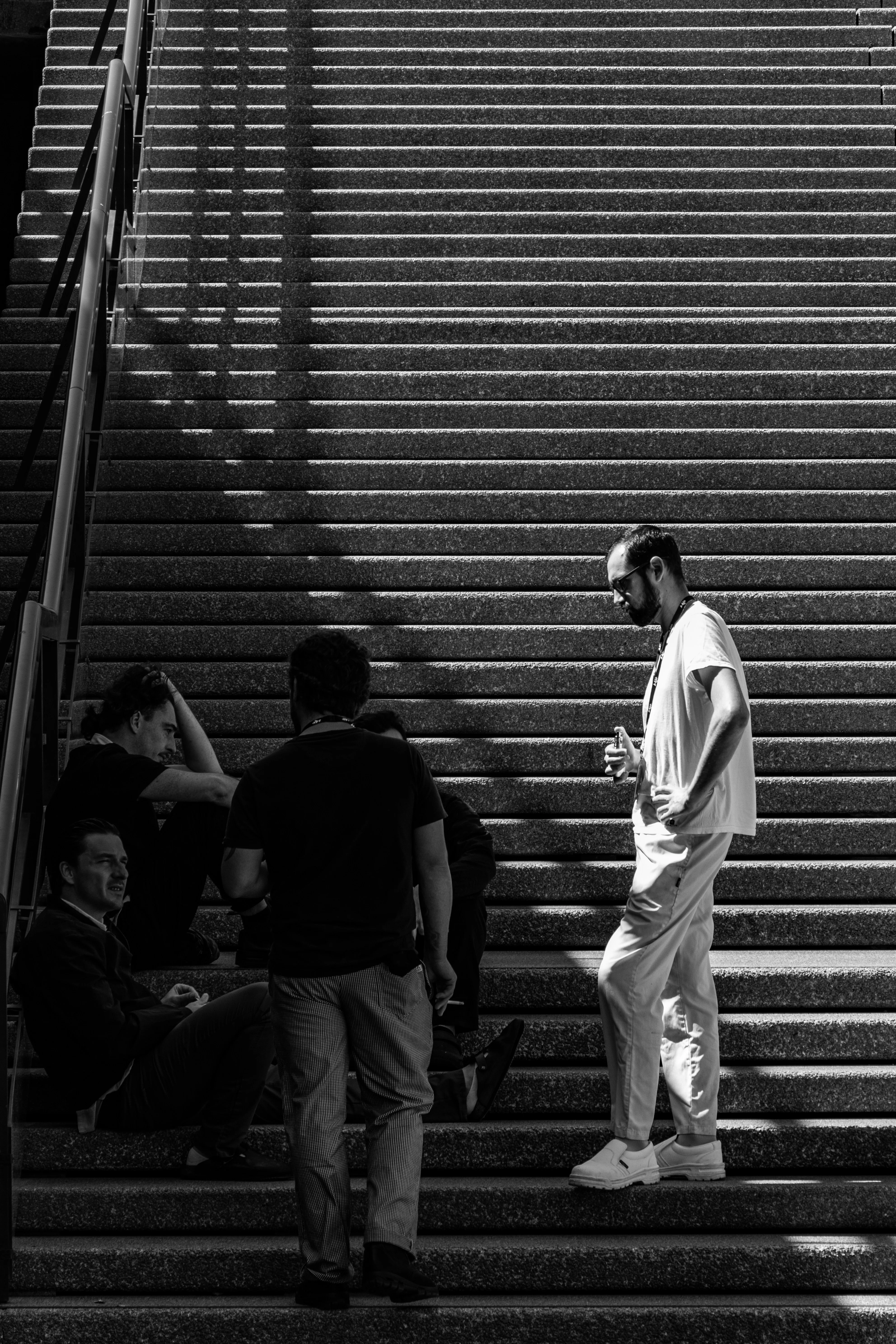 Three men on a wide staircase at different levels, one standing, one walking, one sitting — none quite together