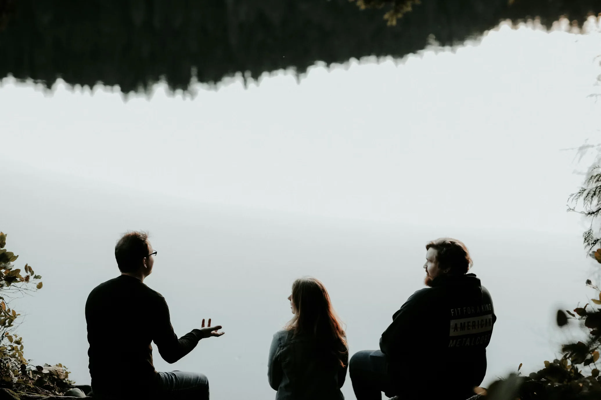 Silhouette of three people sitting on cliff under foggy weather